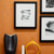 Cluster of black and white abstract art framed with white mats and black frames on an orange wall. Bountiful Framing